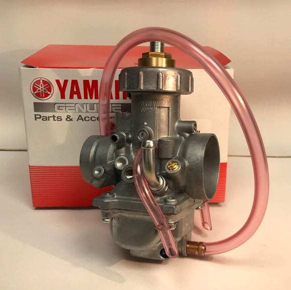 This image shows a Yamaha genuine carburetor assembly, part number 2GU-14102-01, displayed in front of its red and white product box. The carburetor is made of metal with a silver finish and features multiple connection points, adjustment screws, and an attached clear pink fuel line. The assembly is designed for precision mixing of air and fuel for internal combustion engines.